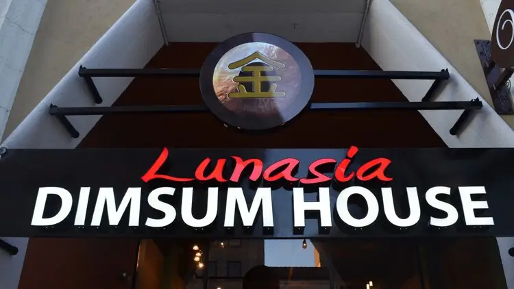 Storefront sign for "Lunasia Dimsum House." The sign features the name "Lunasia" in red cursive letters above "Dimsum House" in white block letters on a black background. Above the sign is a round logo with a stylized gold character on it.